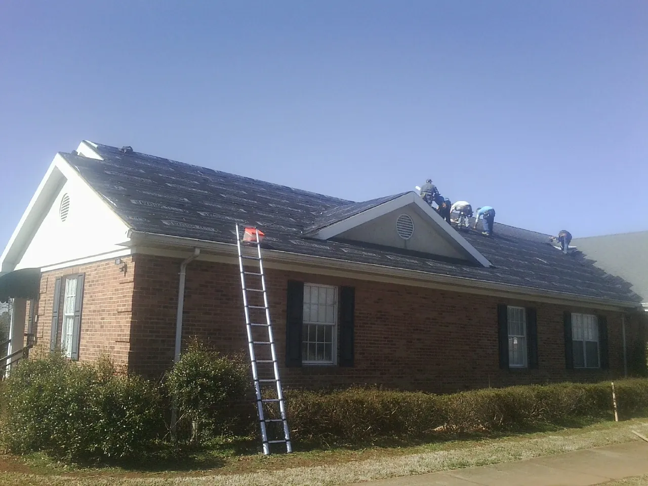 Crew tearing shingles off a brick ranch roof with a ladder set — Metal Roof Repair work by our crew in Arnaudville