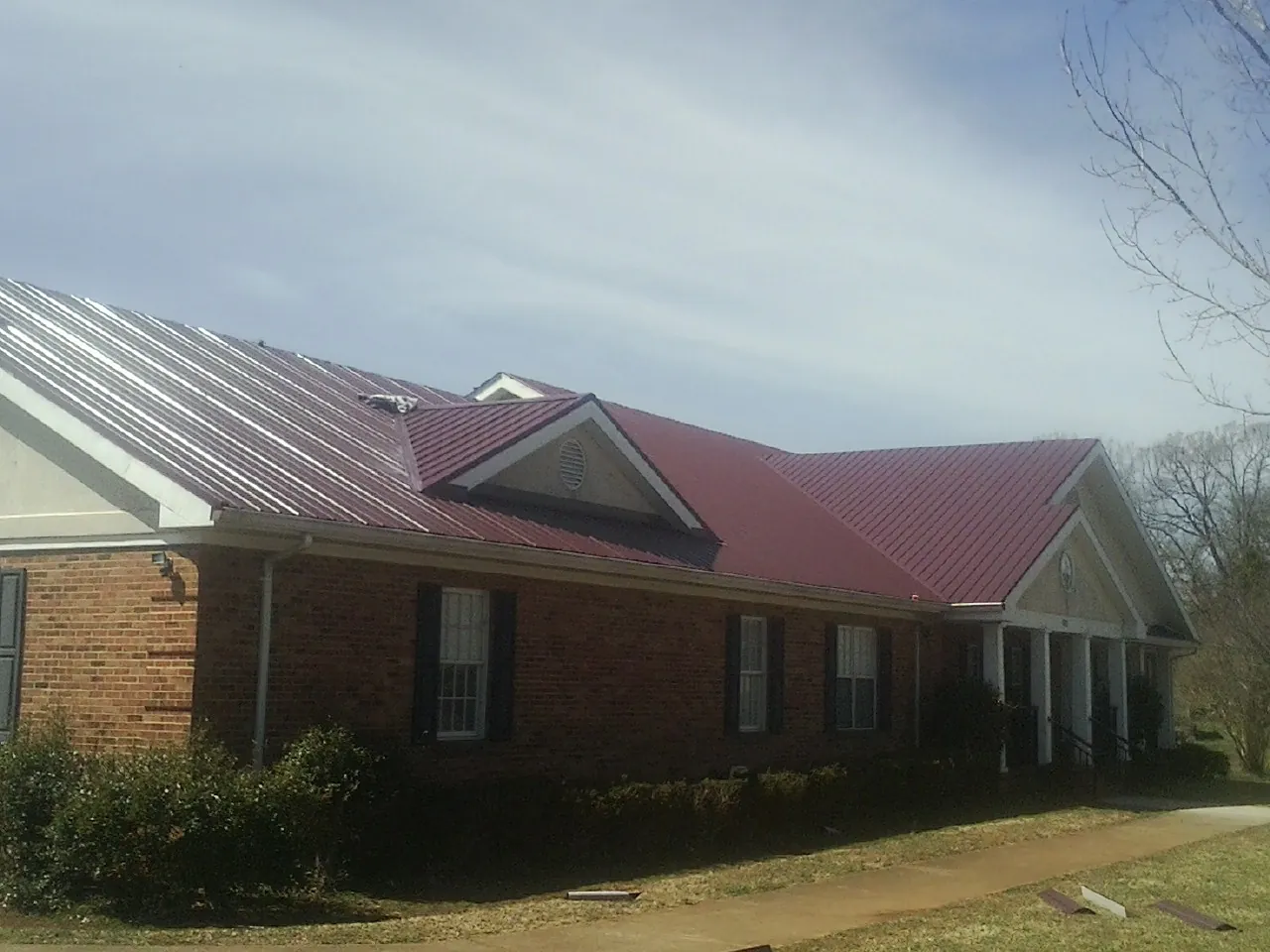 Red metal roof with gabled entries on a long brick building, from a Hail Damage Roof Repair job in Arnaudville