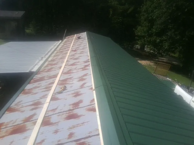 Old rusted panels beside newly installed green metal roofing — Wind Damage Roof Repair by Roofing Brothers in Arnaudville