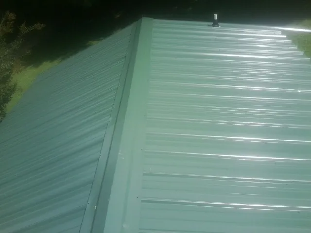 New green metal panels meeting at the ridge of a roof — Flat Roof Repair work by our crew in Arnaudville