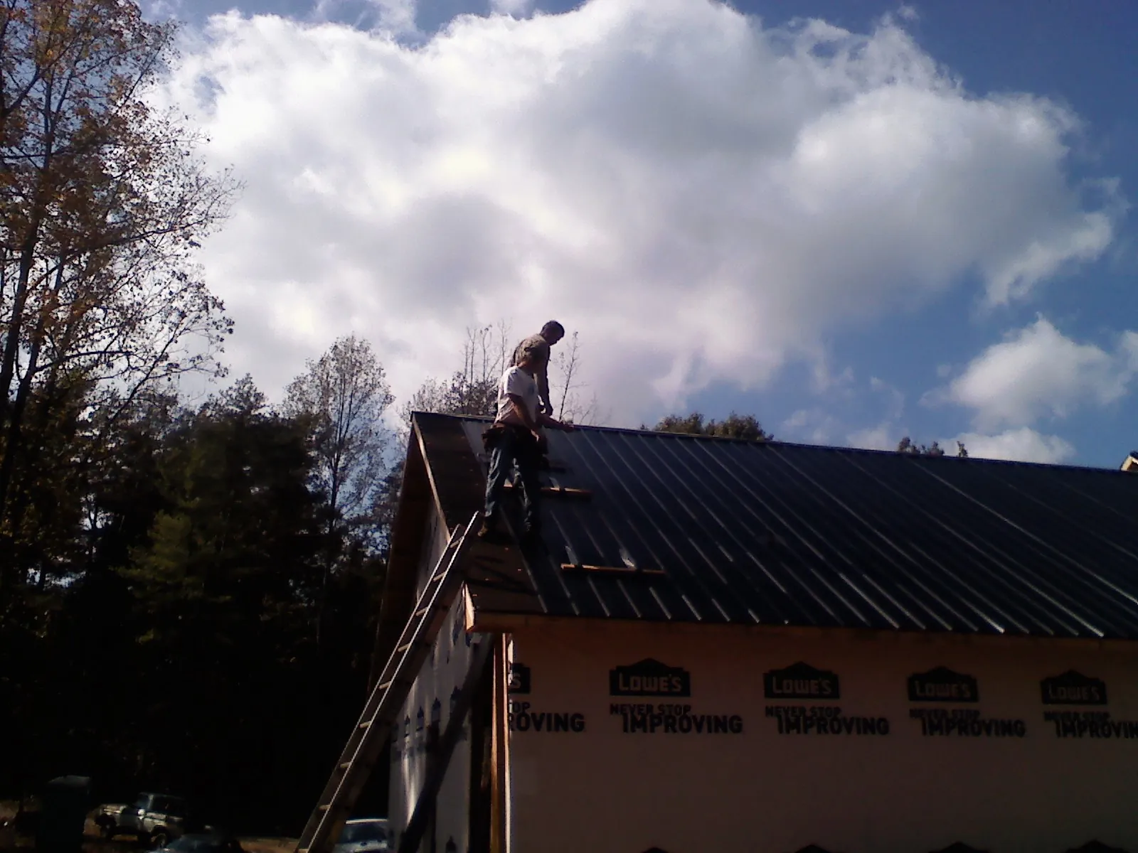 Roofer fastening dark metal panels high against a cloudy sky, from a Roof Inspection job in Arnaudville