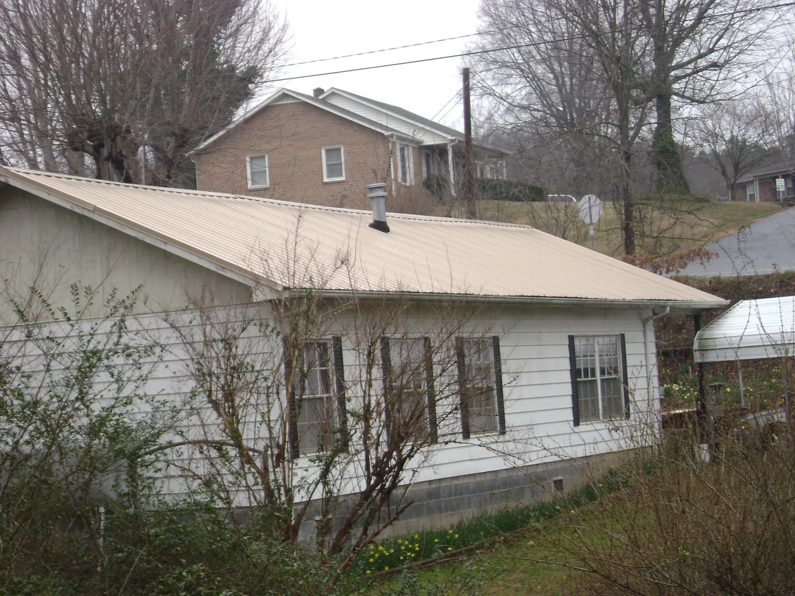 Tan metal roof on a white sided house set into a hillside — Commercial Roofing by Roofing Brothers in Arnaudville