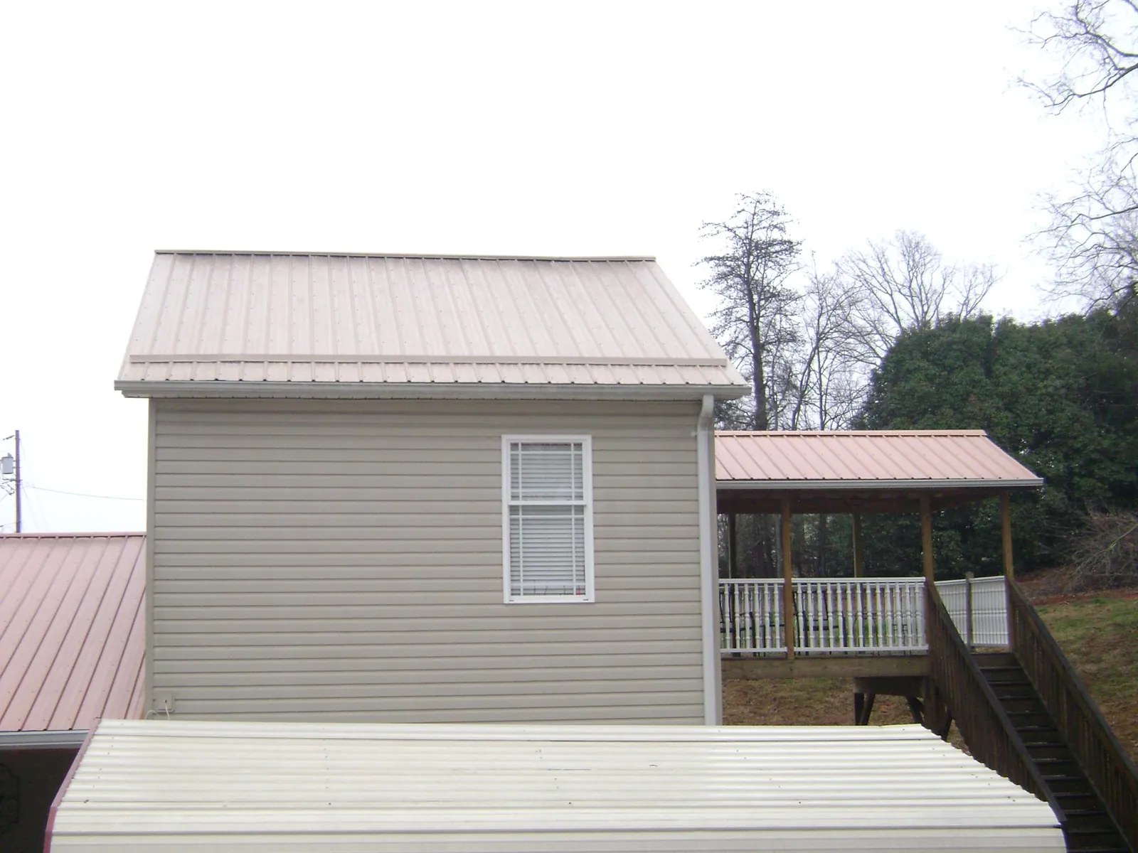 Tan metal roofs on a two story addition and attached porch, from a Roof Replacement job in Arnaudville